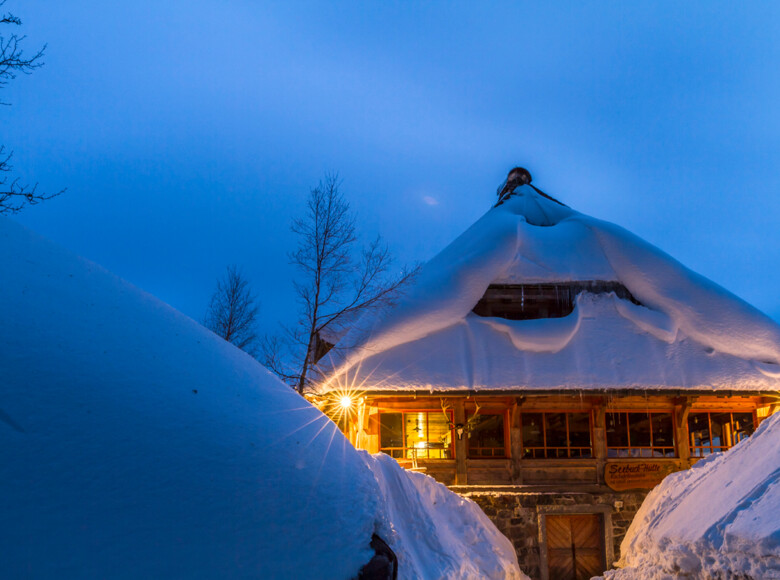 Zwischen den hohen Schneehügeln sieht die Hütte aus wie ein gestrandetes Holzschiff.